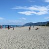 Una spiaggia affollata con mare e montagne.