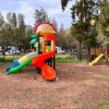 Parco giochi con scivolo colorato e strutture in legno tra gli alberi.