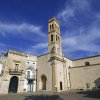 Chiesa storica con torre campanaria sotto un cielo blu e nuvole.